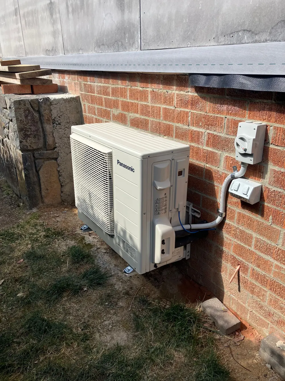Outdoor heat pump unit mounted beside a brick wall